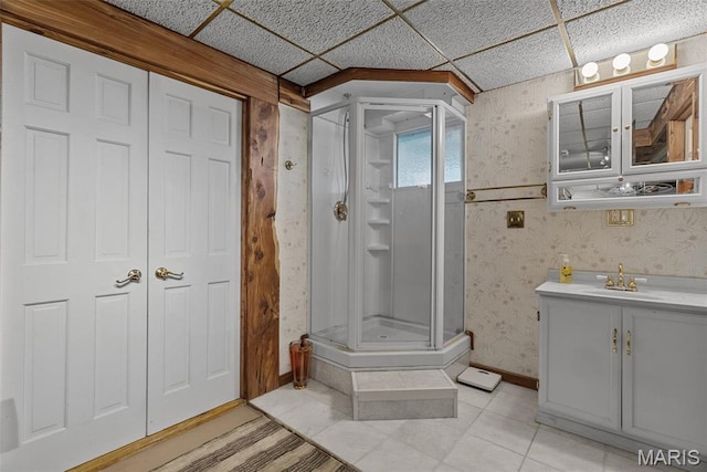 bathroom featuring wallpapered walls, a stall shower, a paneled ceiling, tile patterned floors, and vanity