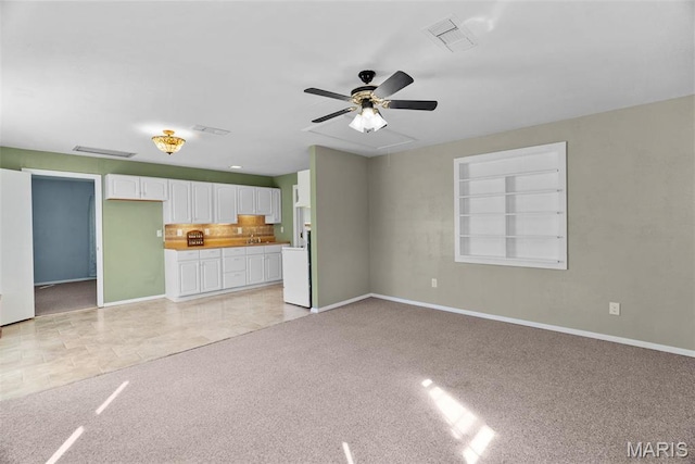 unfurnished living room featuring baseboards, light colored carpet, a ceiling fan, and attic access