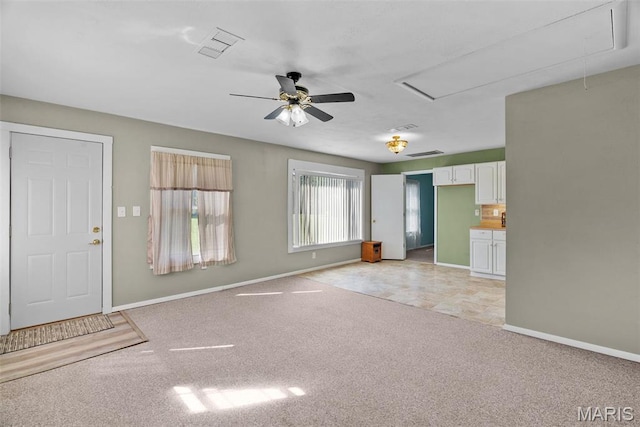 unfurnished living room with attic access, a ceiling fan, light colored carpet, and baseboards