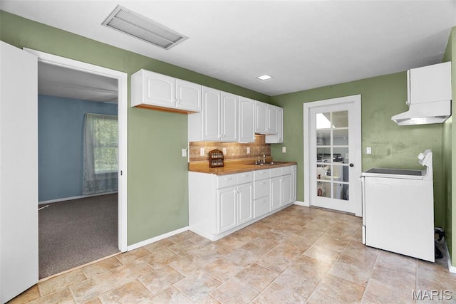 kitchen with white cabinetry, decorative backsplash, a sink, under cabinet range hood, and baseboards