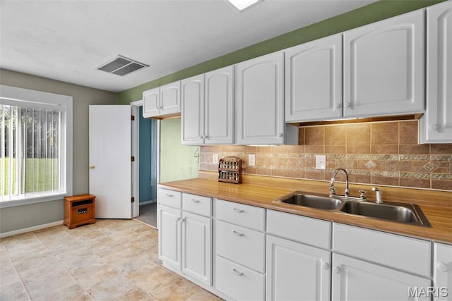 kitchen with a sink, baseboards, tasteful backsplash, and white cabinetry