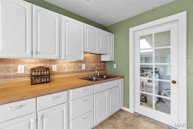 kitchen with a sink, tasteful backsplash, white cabinetry, and light countertops