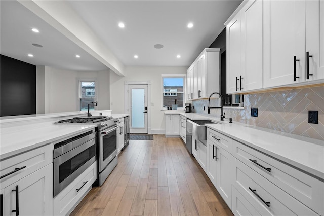 5818 Westminster Pl, Saint Louis, MO 63112 - kitchen featuring a sink, stainless steel appliances, decorative backsplash, white cabinetry, and healthy amount of natural light