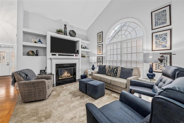 living area with high vaulted ceiling, wood finished floors, a premium fireplace, and built in features