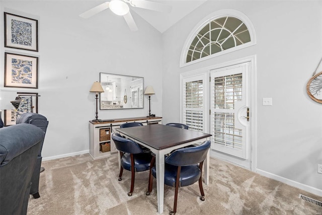 dining space with light colored carpet, a ceiling fan, baseboards, and high vaulted ceiling
