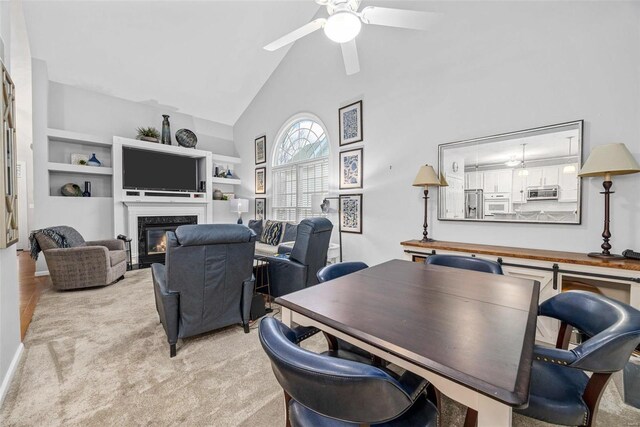 office area featuring high vaulted ceiling, a ceiling fan, a high end fireplace, light carpet, and built in shelves