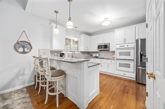 kitchen with appliances with stainless steel finishes, a peninsula, white cabinets, and decorative backsplash