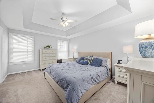 bedroom featuring light colored carpet, a raised ceiling, baseboards, and ceiling fan
