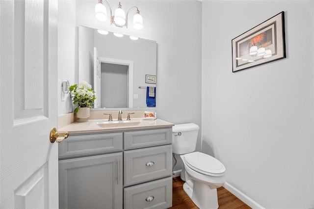 half bathroom with wood finished floors, vanity, toilet, baseboards, and a chandelier