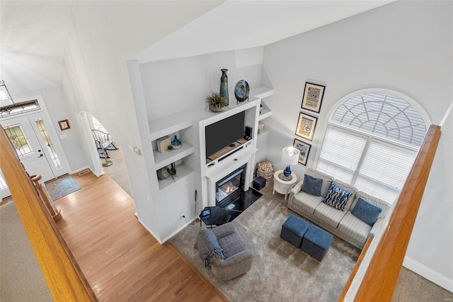 living area featuring healthy amount of natural light, wood finished floors, a glass covered fireplace, built in shelves, and a towering ceiling