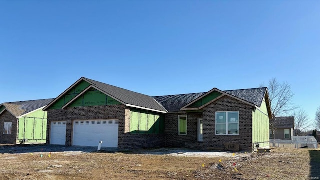 view of front facade with an attached garage, brick siding, fence, and a shingled roof