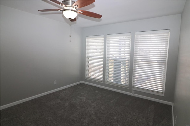 empty room with dark colored carpet, baseboards, and a ceiling fan