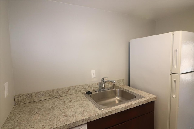 kitchen with a sink, freestanding refrigerator, light countertops, and dark brown cabinetry