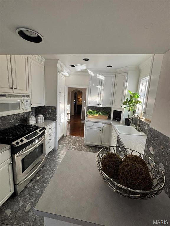 7810 Lafon Pl, University City, MO 63130 - kitchen featuring white microwave, a sink, gas range, arched walkways, and crown molding