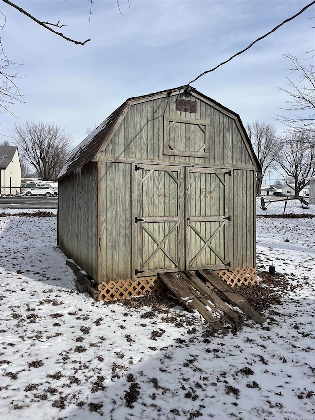 snow covered structure featuring a storage unit, an outbuilding, and fence