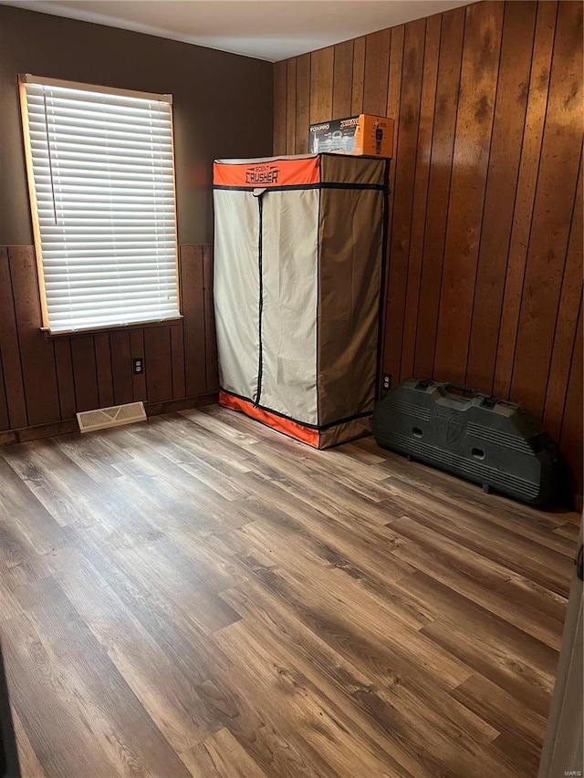 unfurnished bedroom with wooden walls, wood finished floors, and a wainscoted wall