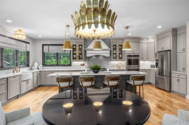 130 Foristell Ridge Ct, Foristell, MO 63348 - kitchen with appliances with stainless steel finishes, gray cabinetry, custom exhaust hood, backsplash, and a kitchen bar