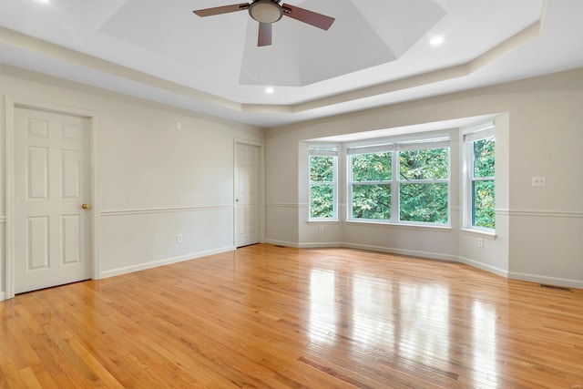 spare room with a tray ceiling, ceiling fan, light wood-style floors, baseboards, and recessed lighting