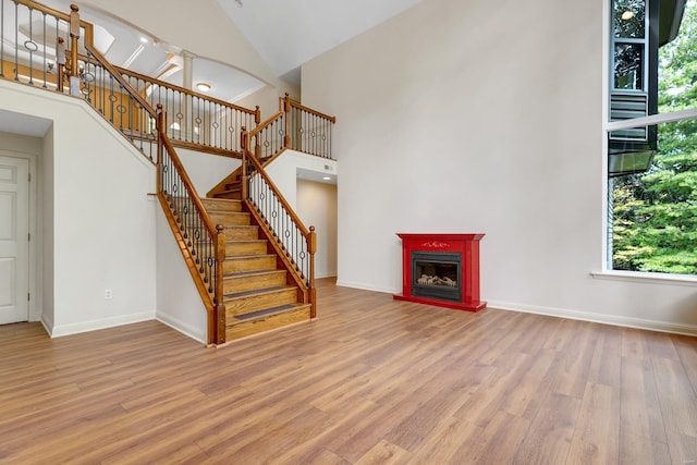 unfurnished living room featuring a towering ceiling, light wood finished floors, stairway, and baseboards