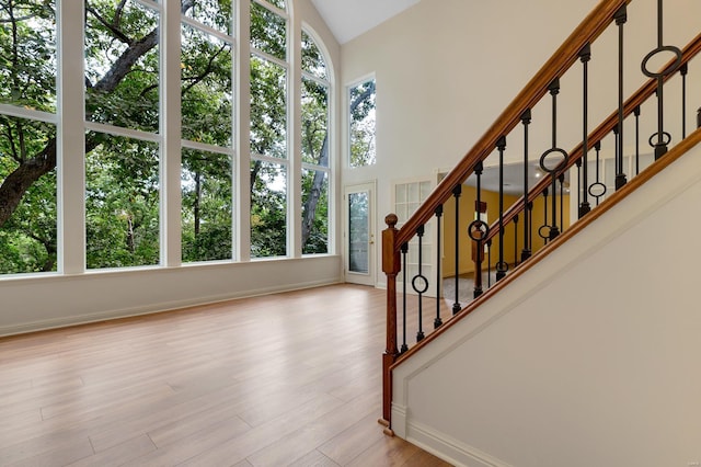 staircase with baseboards, wood finished floors, and high vaulted ceiling