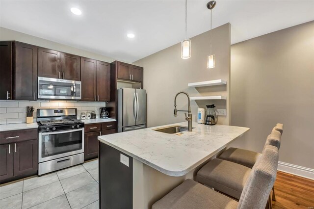 kitchen featuring appliances with stainless steel finishes, a sink, dark brown cabinets, a kitchen bar, and recessed lighting