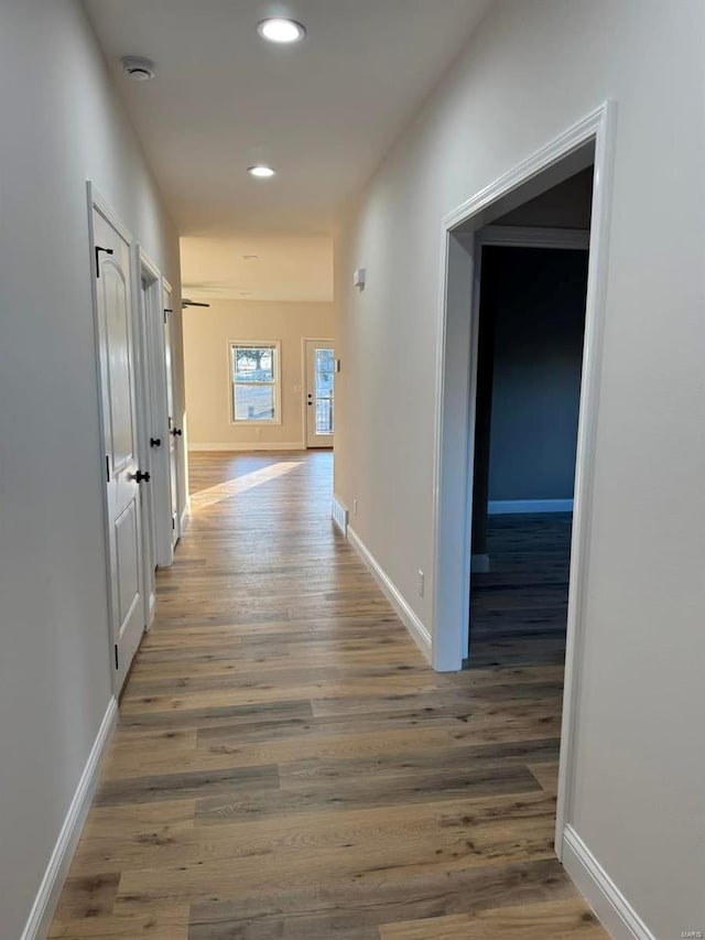 corridor with wood finished floors, recessed lighting, and baseboards