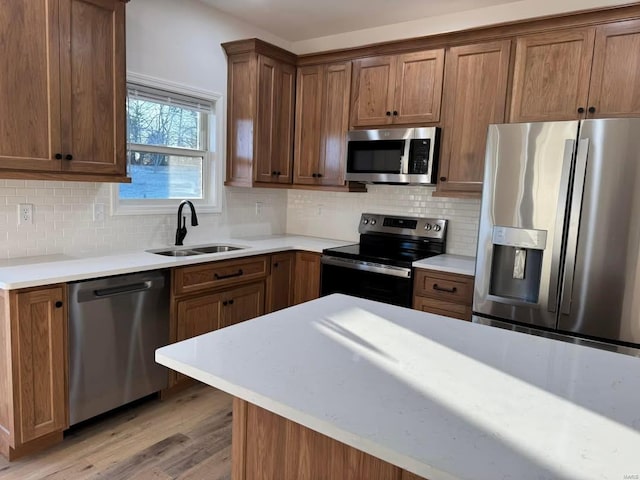 kitchen featuring stainless steel appliances, a sink, light wood finished floors, and decorative backsplash