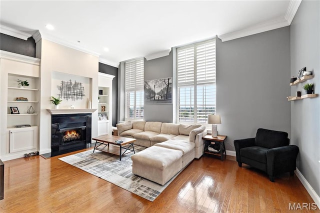 living area with ornamental molding, wood finished floors, baseboards, a fireplace with flush hearth, and built in shelves