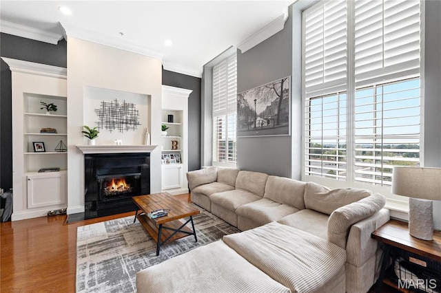 living area with crown molding, built in features, a fireplace with flush hearth, wood finished floors, and recessed lighting