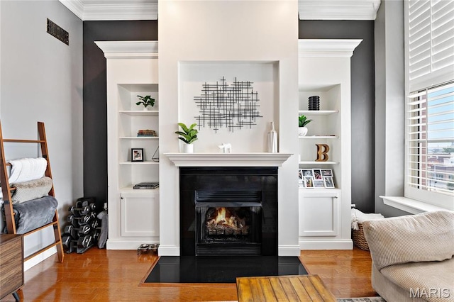 living area featuring wood finished floors, built in features, a fireplace with flush hearth, and crown molding