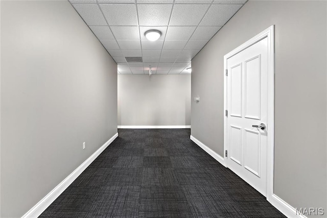 corridor with dark carpet, baseboards, and a paneled ceiling