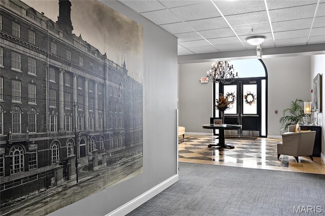 corridor with baseboards, a chandelier, a paneled ceiling, and carpet flooring