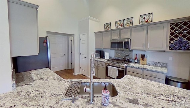 112 Summit Rdg, Maryville, IL 62062 - kitchen featuring gray cabinetry, stainless steel appliances, wood finished floors, a towering ceiling, and light stone countertops
