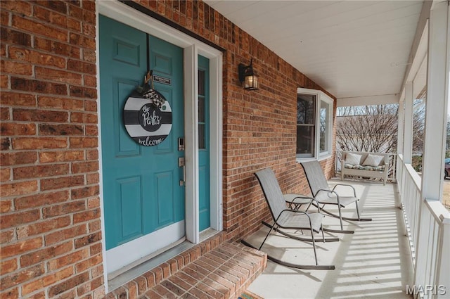 doorway to property with covered porch and brick siding