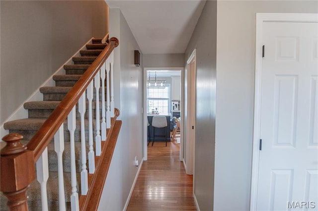 staircase featuring wood finished floors, baseboards, and a chandelier