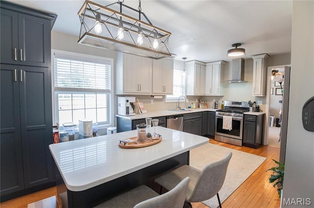 kitchen featuring appliances with stainless steel finishes, wall chimney range hood, a sink, light countertops, and a breakfast bar area
