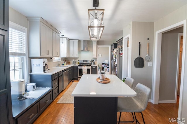 kitchen featuring stainless steel appliances, a sink, wall chimney range hood, a kitchen island, and light wood-type flooring