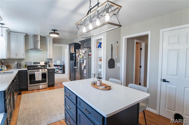 kitchen with wall chimney exhaust hood, stainless steel appliances, blue cabinets, and light countertops