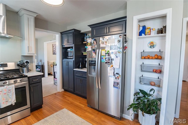 kitchen featuring appliances with stainless steel finishes, wall chimney range hood, light wood-type flooring, and light countertops