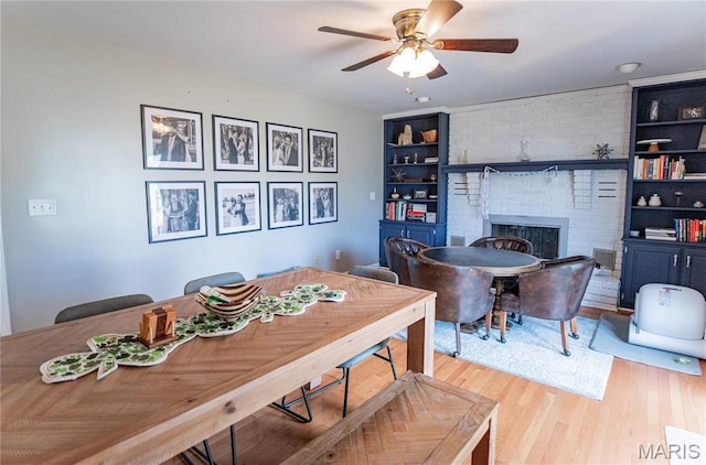 dining space with a ceiling fan, wood finished floors, a brick fireplace, and built in features