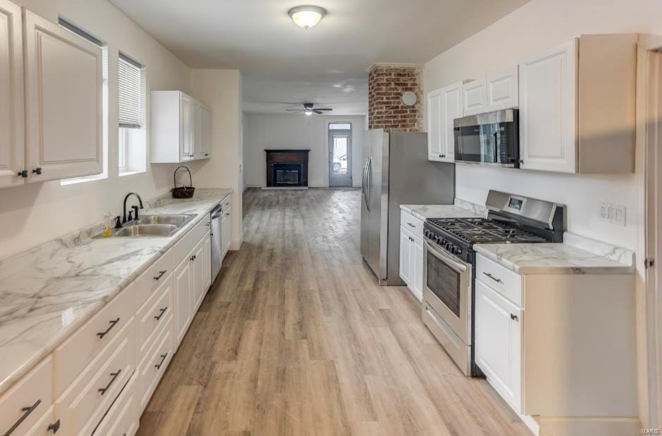 kitchen with appliances with stainless steel finishes, a sink, ceiling fan, open floor plan, and light wood-style flooring