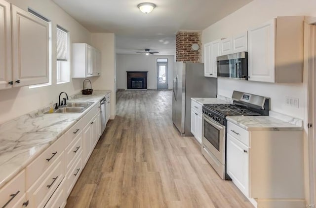 kitchen with appliances with stainless steel finishes, a sink, ceiling fan, open floor plan, and light wood-style flooring