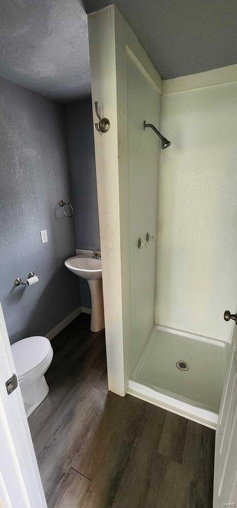 bathroom featuring a stall shower, wood finished floors, toilet, a textured ceiling, and baseboards