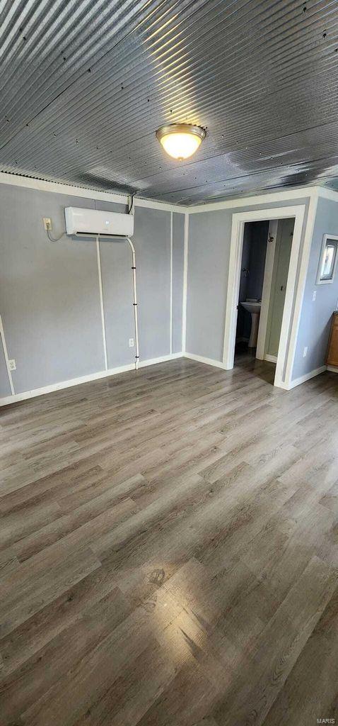 below grade area with an AC wall unit, wood finished floors, and baseboards