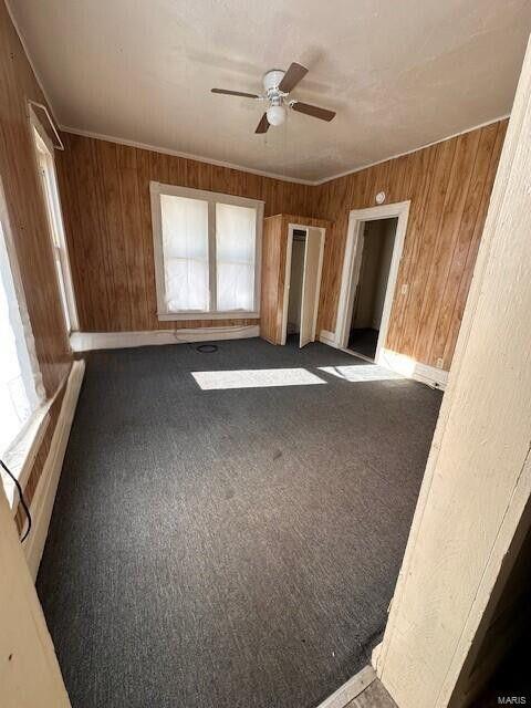 unfurnished room featuring wooden walls, a ceiling fan, dark colored carpet, and baseboards