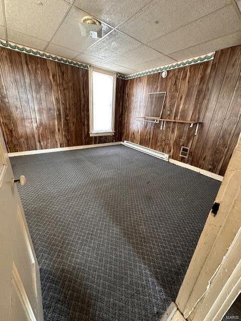 carpeted empty room with wooden walls, baseboards, and a paneled ceiling