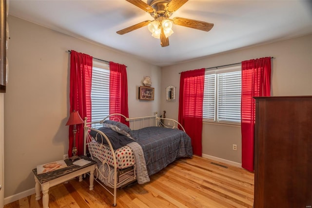 bedroom with multiple windows, wood finished floors, ceiling fan, and baseboards