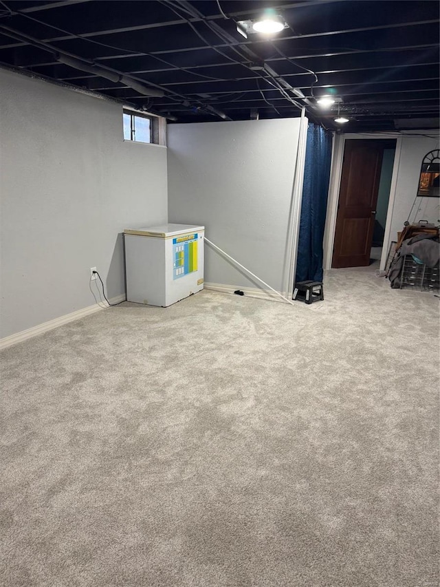 below grade area featuring carpet flooring, baseboards, and fridge