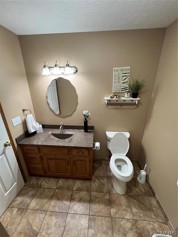 half bathroom with toilet, vanity, a textured ceiling, and tile patterned flooring