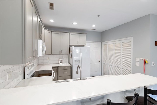 kitchen with white appliances, a sink, a peninsula, backsplash, and recessed lighting